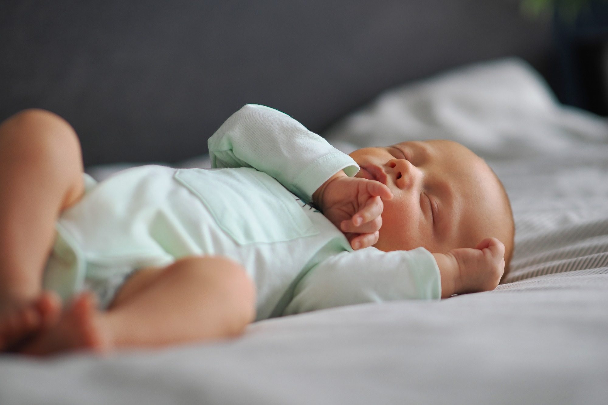 Schlafendes Baby in heller Kleidung, liegt entspannt auf einem Bett.